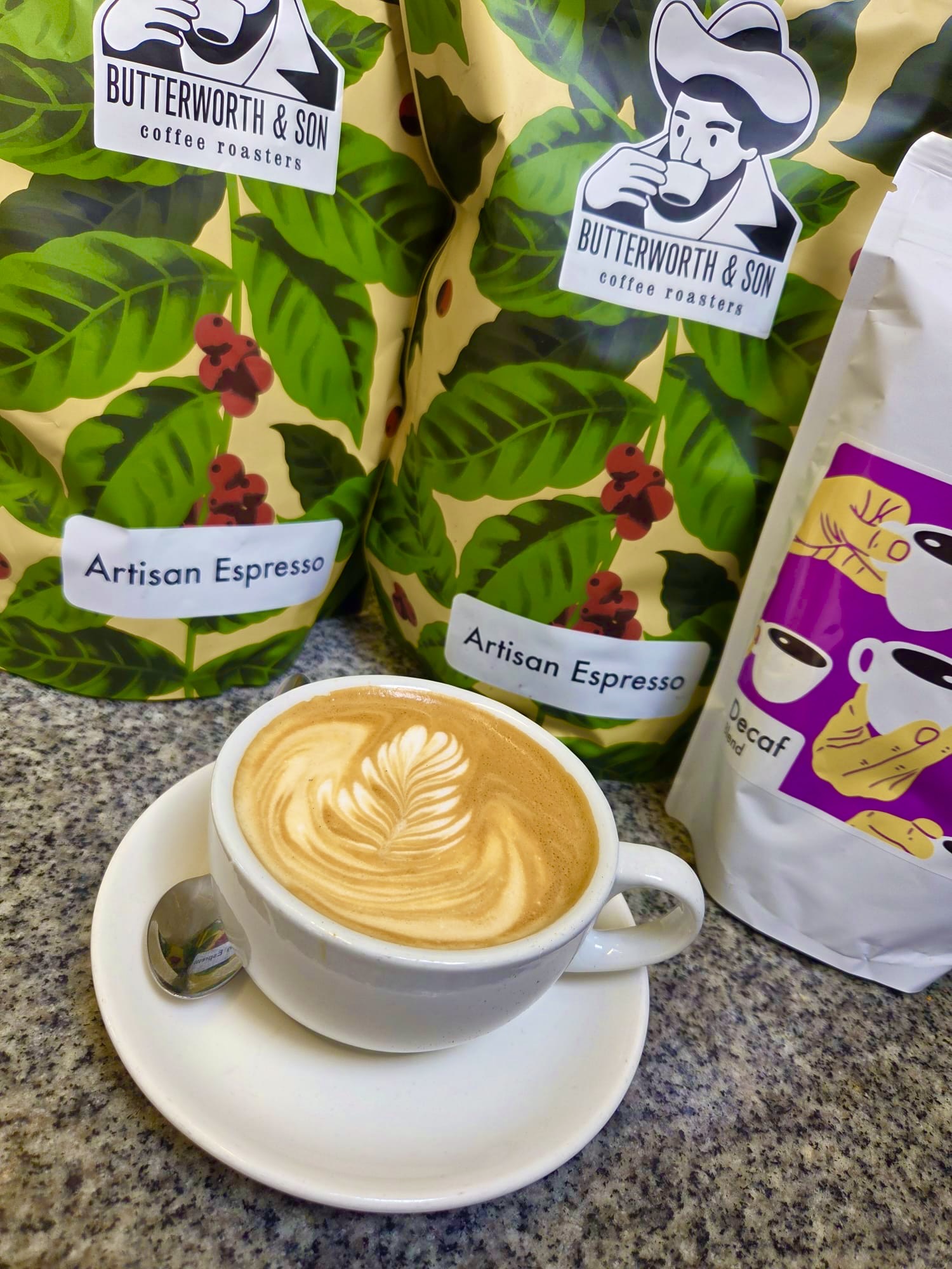A flat white alongside bags of Butterworth & Son coffee